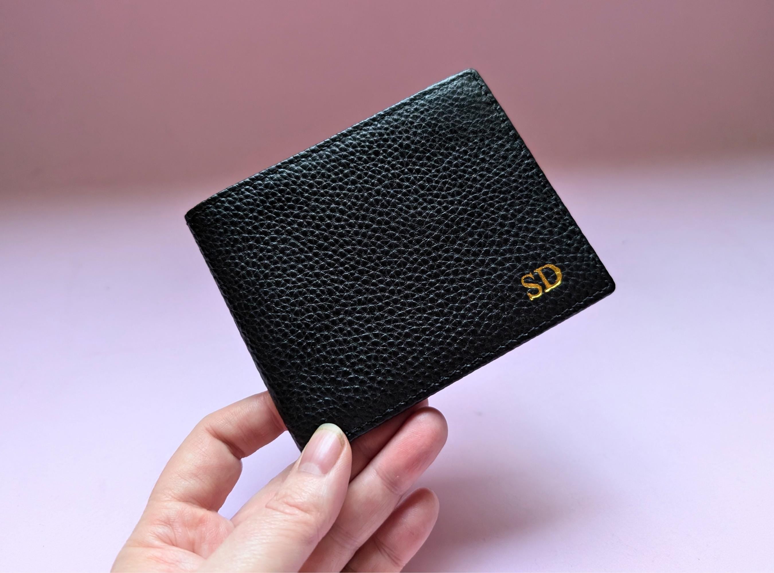 Black pebble leather wallet held by a hand with a pink background