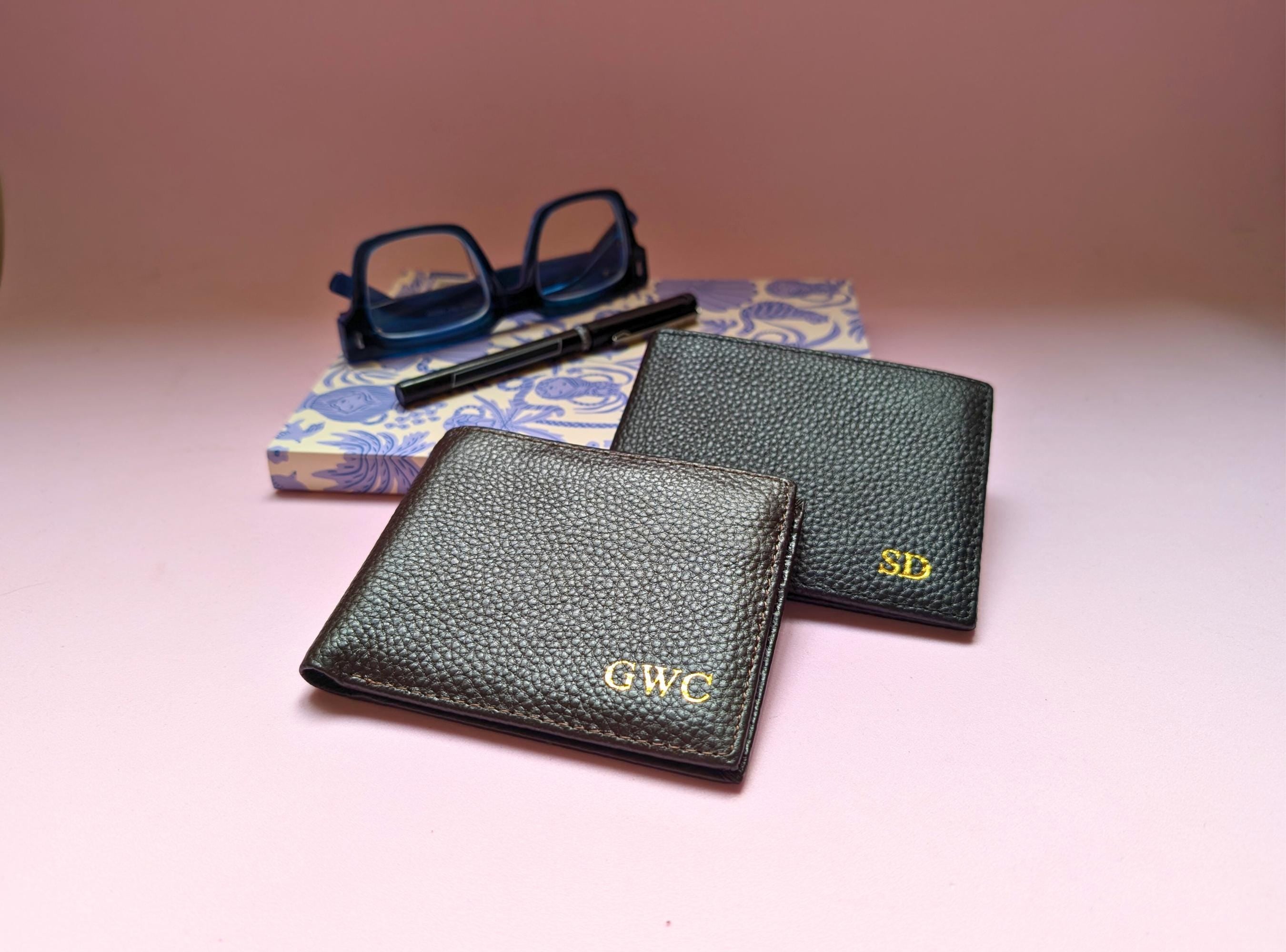 Two genuine leather wallets with custom initials on a pink surface