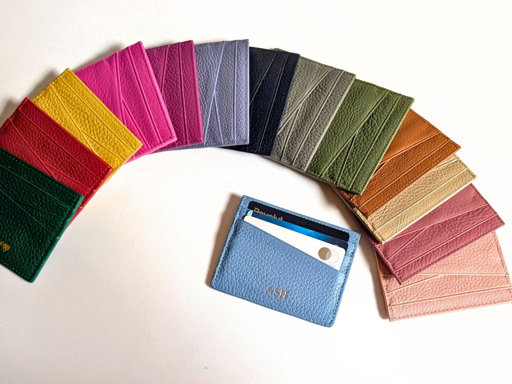 Black textured cardholder with custom intiials, surrounded by colorful cards on a light background