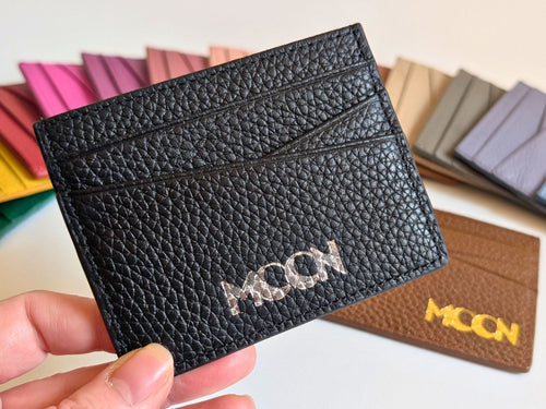 Black textured cardholder with custom branding held by a hand, with other color options in the background showing gold or silver emboss.