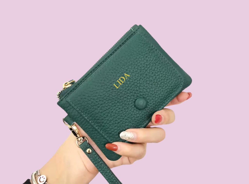 Green wallet with embossed name held by a hand against a light purple background