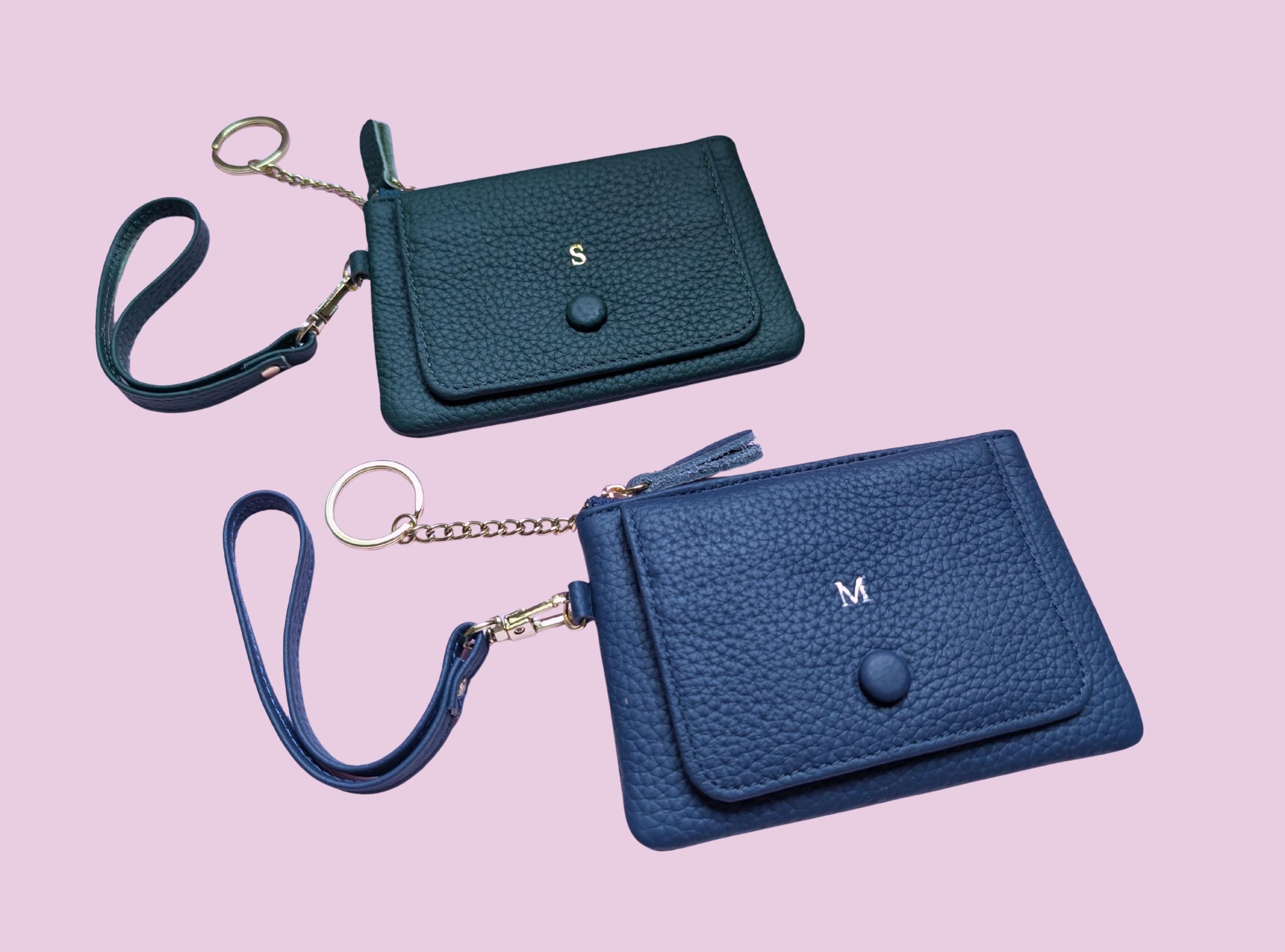 Two blue wallets with wristlets on a pink background
