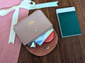 Small pink leather wallet with custom monogram, coins, and cards on a pink surface with a white ribbon.