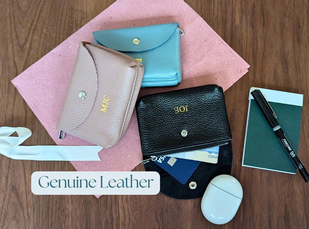 Three small leather wallets on a pink cloth with a pen and notebook on a wooden surface.