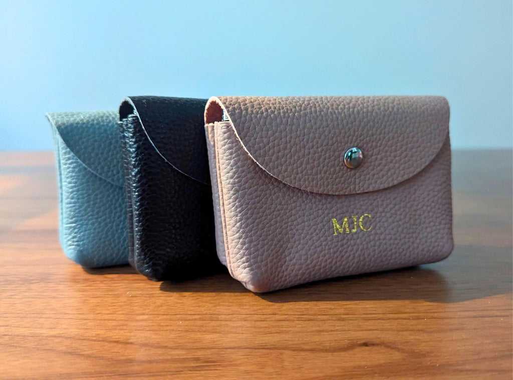 Three small leather pouches in different colors on a wooden surface with a blue background.