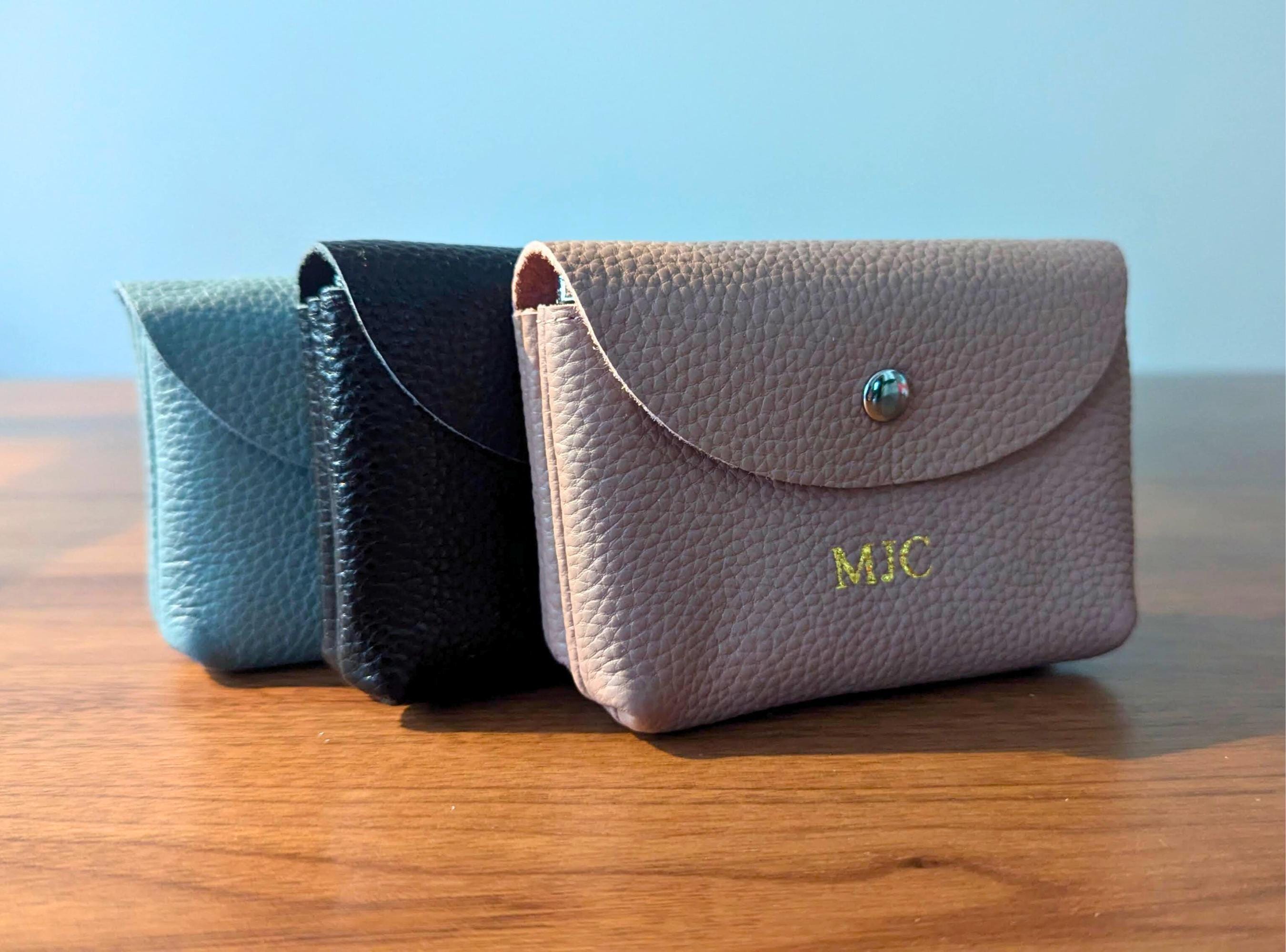 Three small leather pouches in different colors on a wooden surface with a blue background.