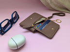 Brown wallet with sunglasses and a mint green case on a pink background