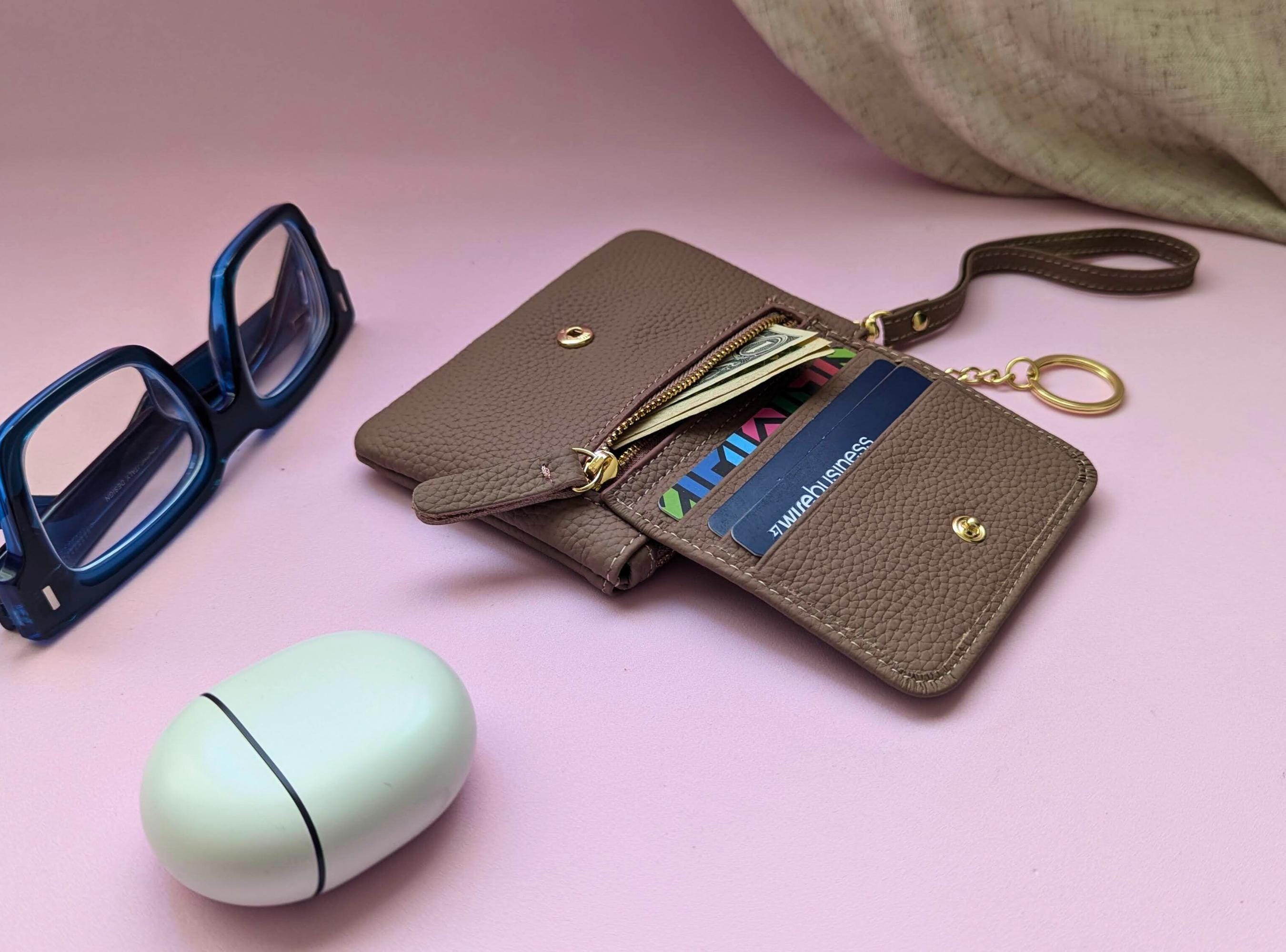 Brown wallet with sunglasses and a mint green case on a pink background