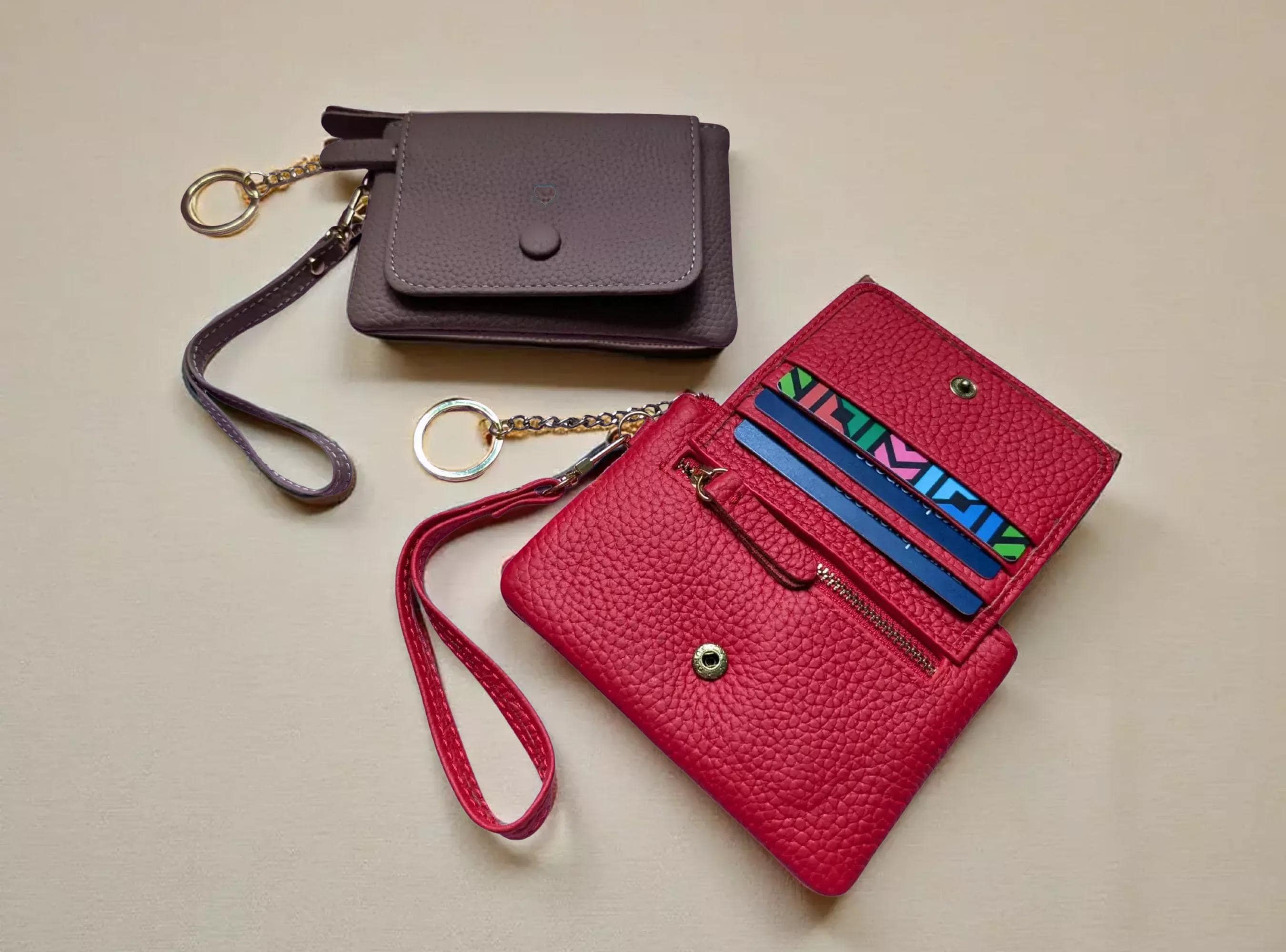 Red leather wallet with wrist strap and smaller purple wallet on a beige background