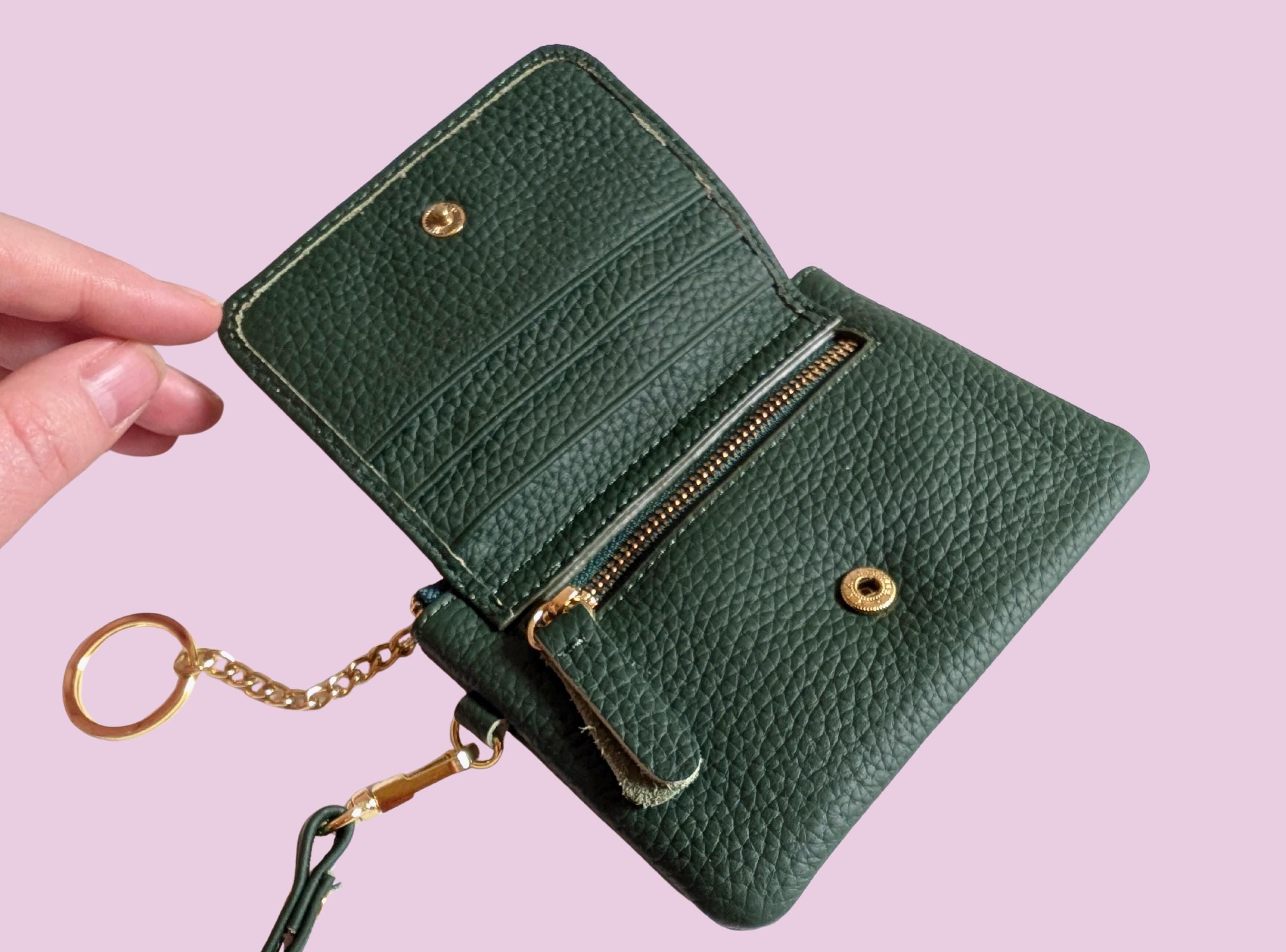 Green leather wallet with gold accents held by a hand on a pink background