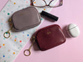 Two small leather pouches with gold chains on a pink and polka dot background.