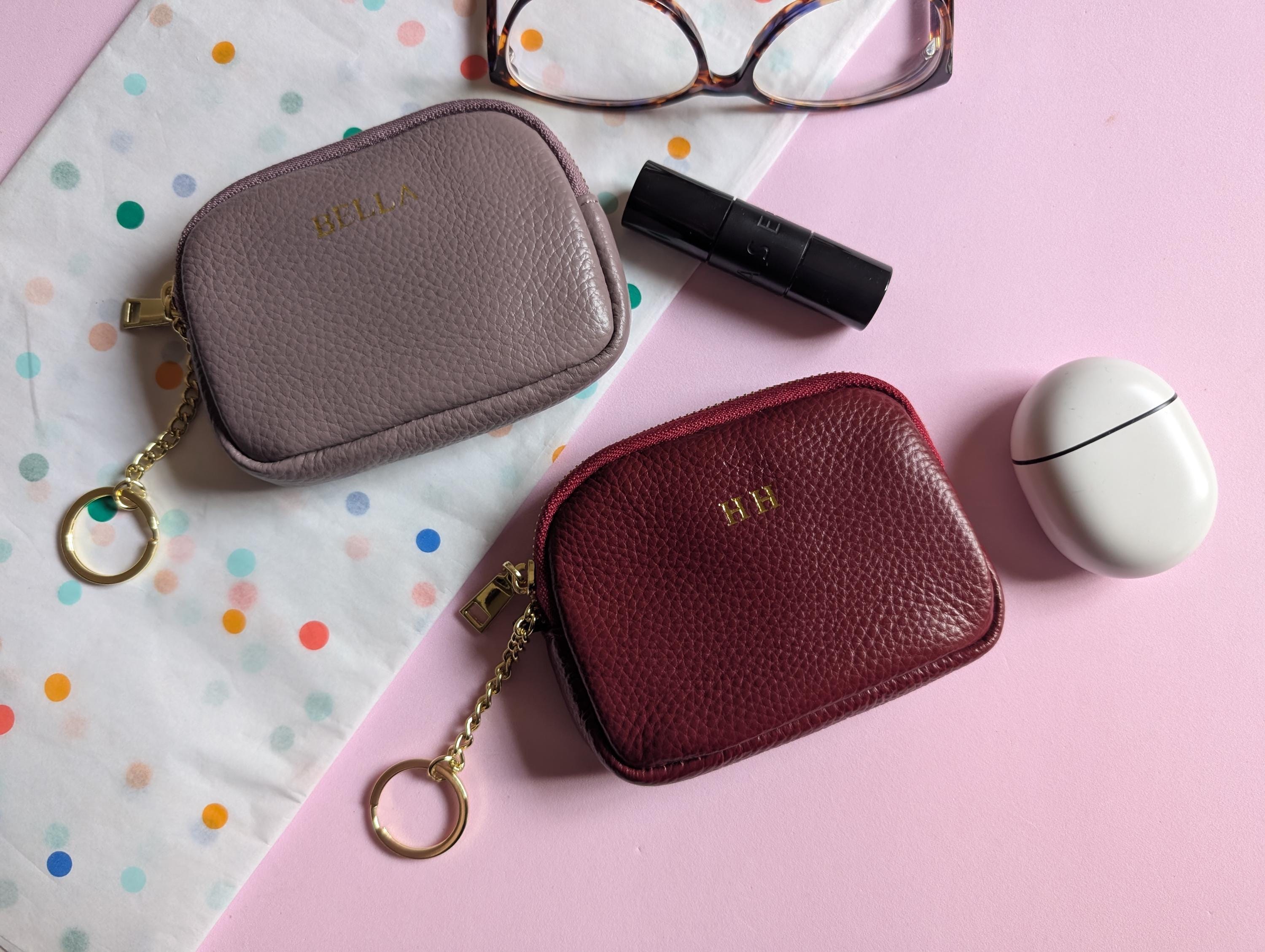Two small leather pouches with gold chains on a pink and polka dot background.