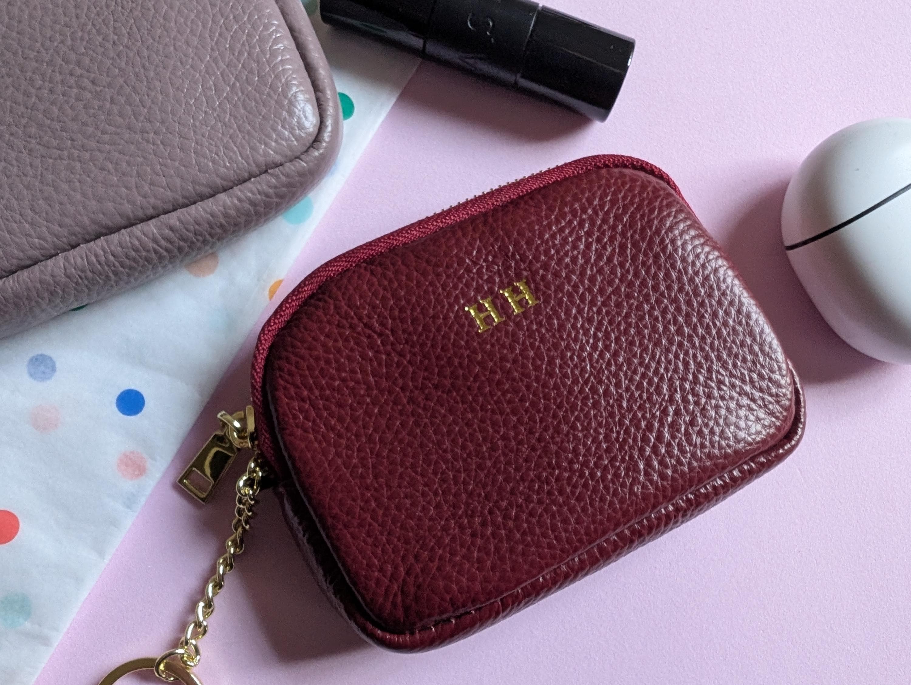 Red leather pouch with gold chain on a pink surface