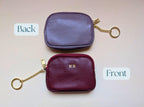 Two purple leather coin purses, one labeled 'Back' and one labeled 'Front', on a light pink background.