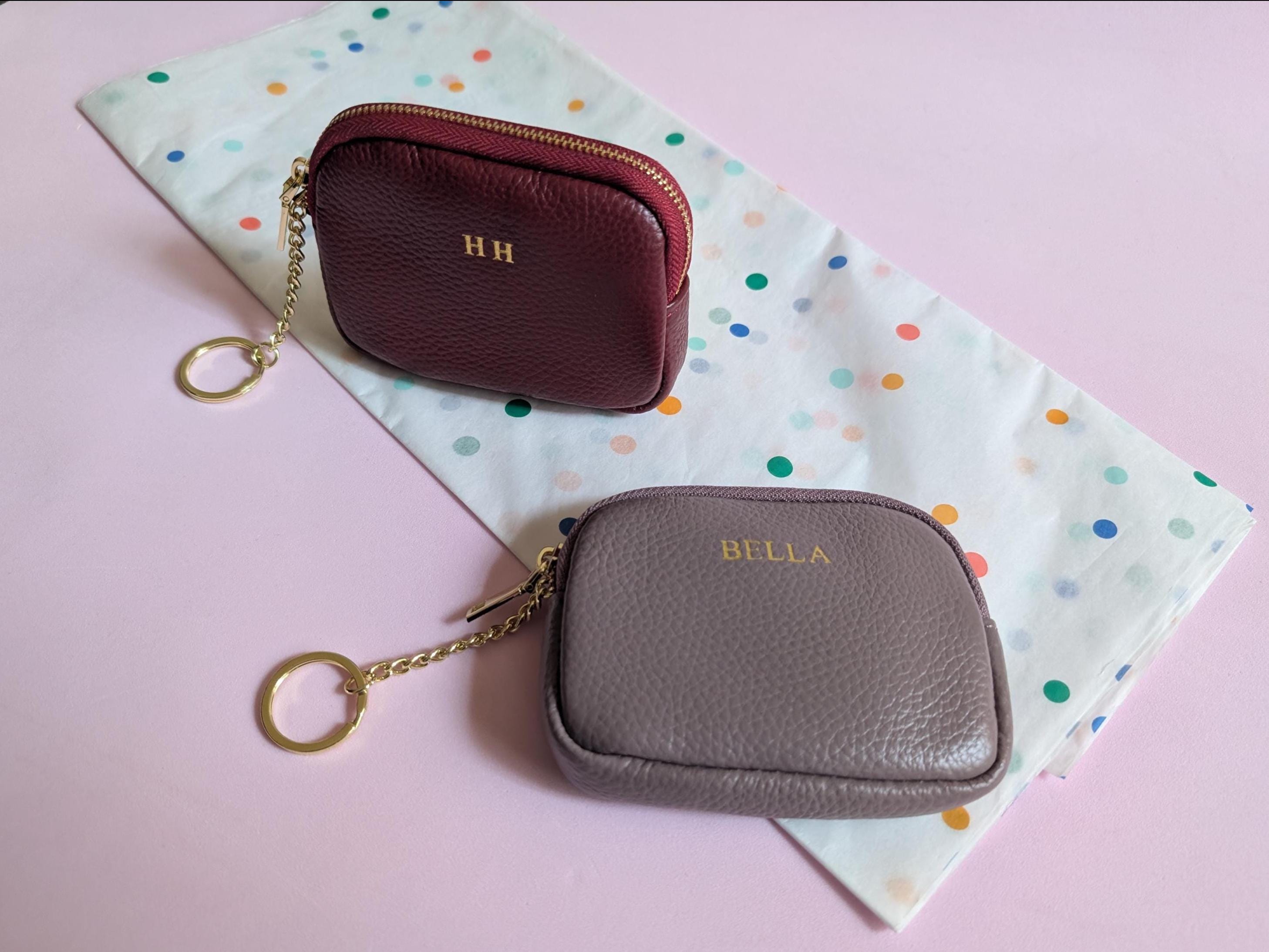 Two small leather pouches, one maroon and one gray, on a polka dot fabric with a pink background.