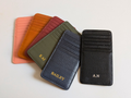Set of five leather card holders in different colors with embossed names on a light background - Pink, Orange, Burgundy, Green, Navy and Black.