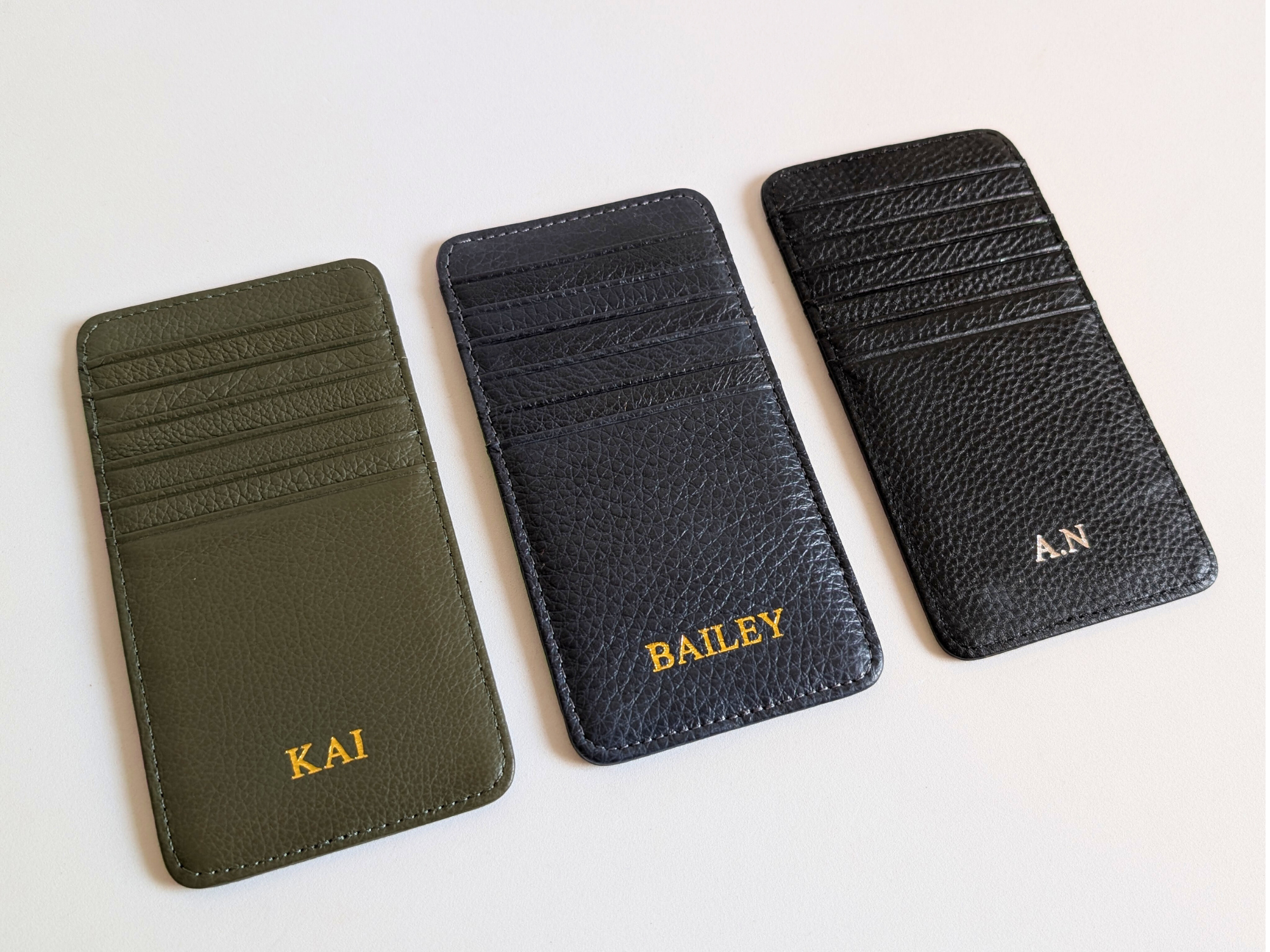 Three leather card holders with personalized names on a white background