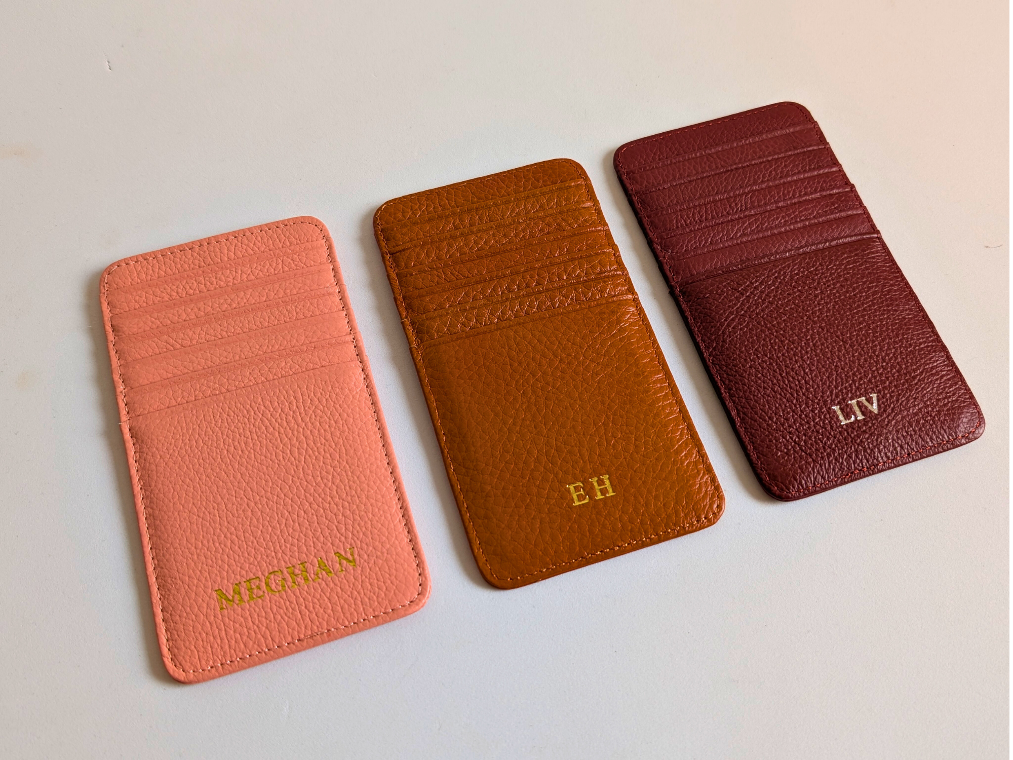 Three leather card holders in different colors with initials engraved on a light background