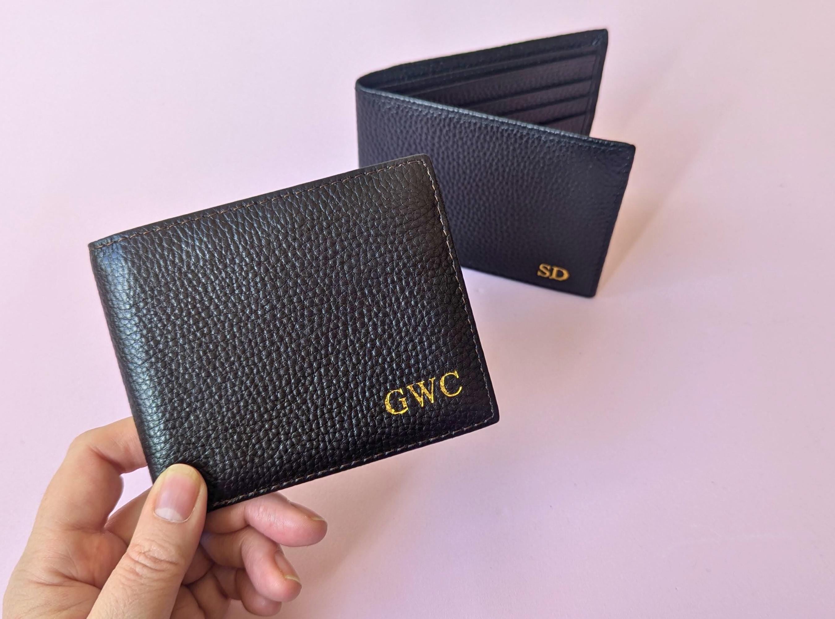 Black leather wallet with custom initials held by a hand on a light pink background