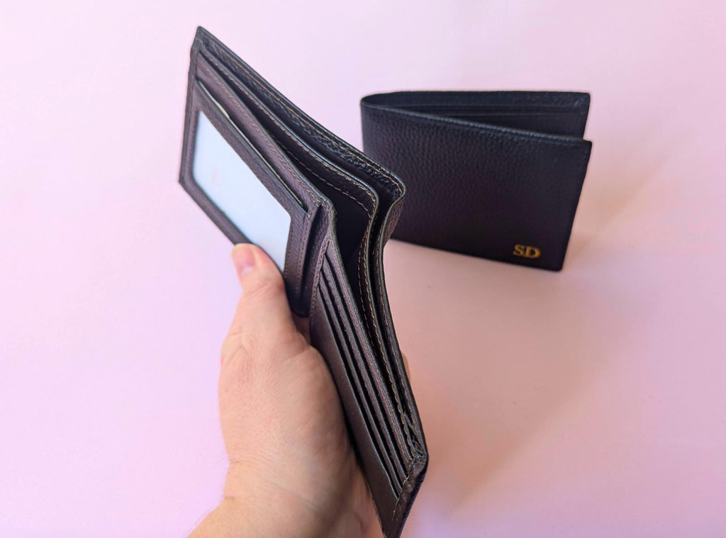 Black wallet held by a hand with another wallet in the background on a pink background