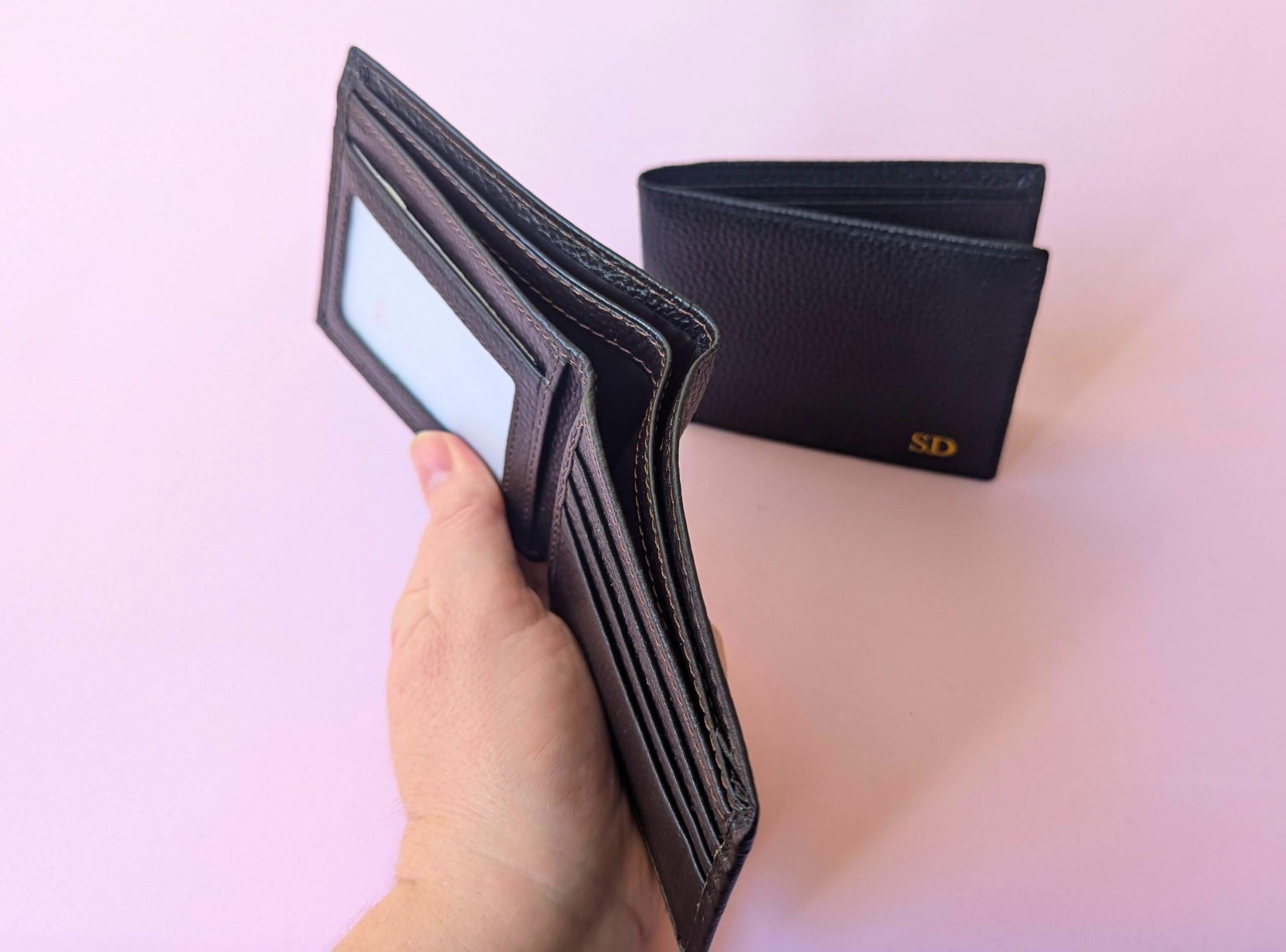 Black wallet held by a hand with another wallet in the background on a pink background
