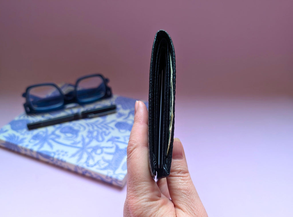 Hand holding a black wallet with glasses and a notebook in the background