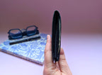 Hand holding a black wallet with glasses and a notebook in the background