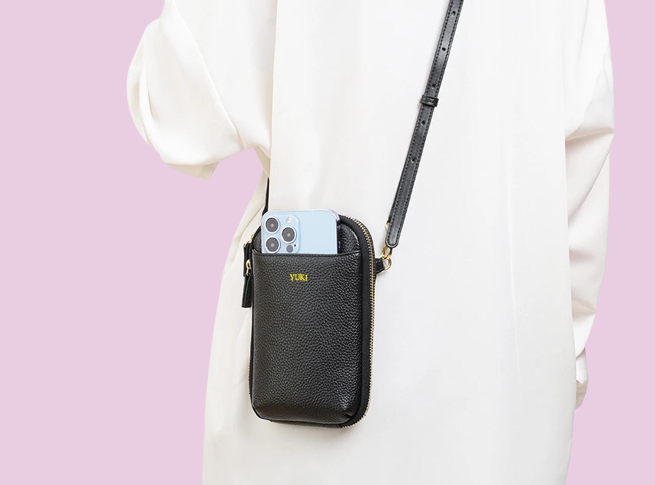Black crossbody bag with a phone case on a pink and white background