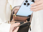 Person placing a smartphone into a black leather handbag with gold zipper.