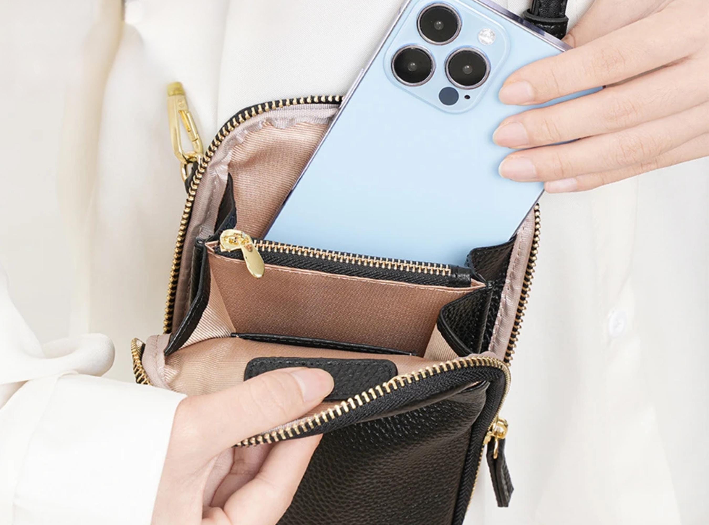 Person placing a smartphone into a black leather handbag with gold zipper.
