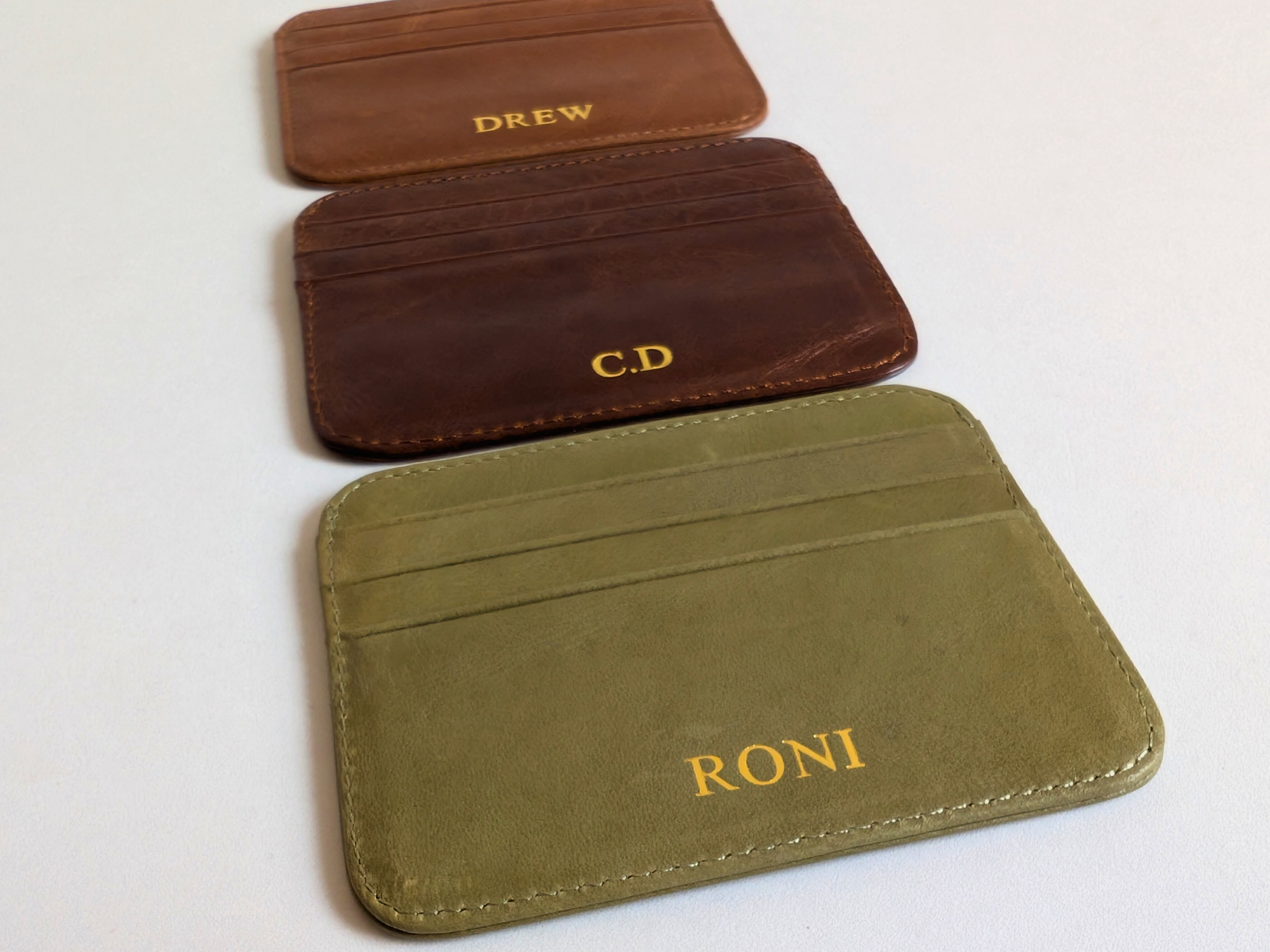 Three leather card holders with personalized names on a white background.