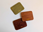 Three leather card holders with engraved names on a light background
