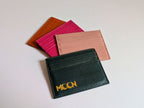Set of colorful leather card holders with a black one featuring 'MOON' branding on a light gray background.