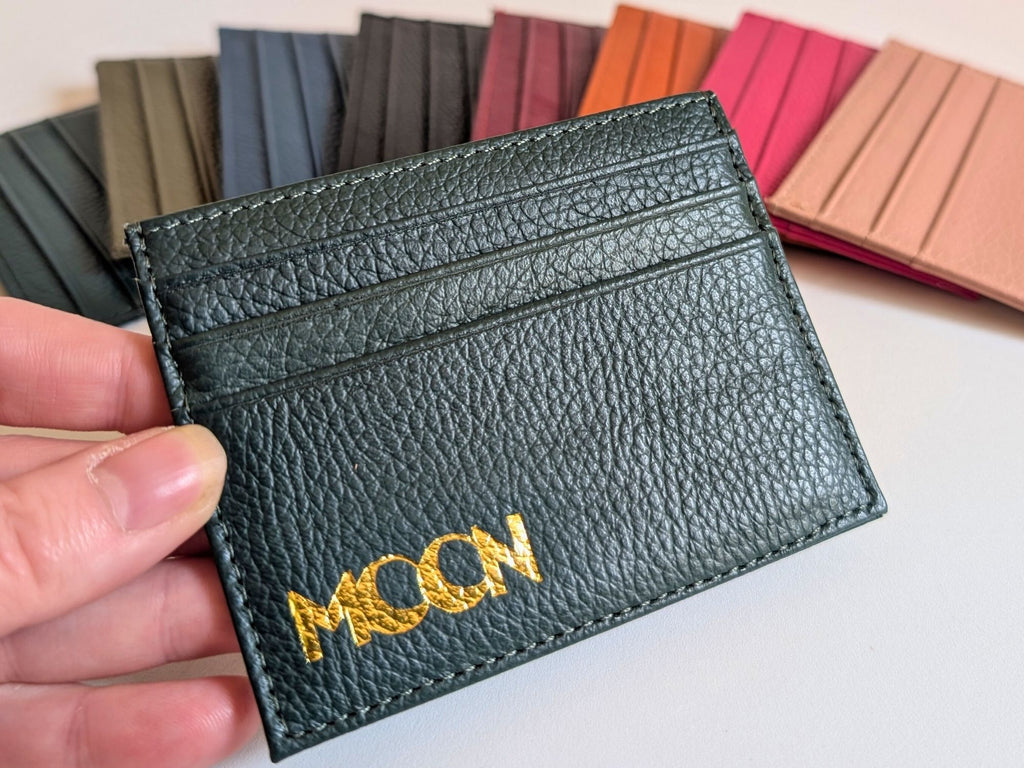 Black leather cardholder with custom emobssed logo held by a hand, with color swatches in the background.