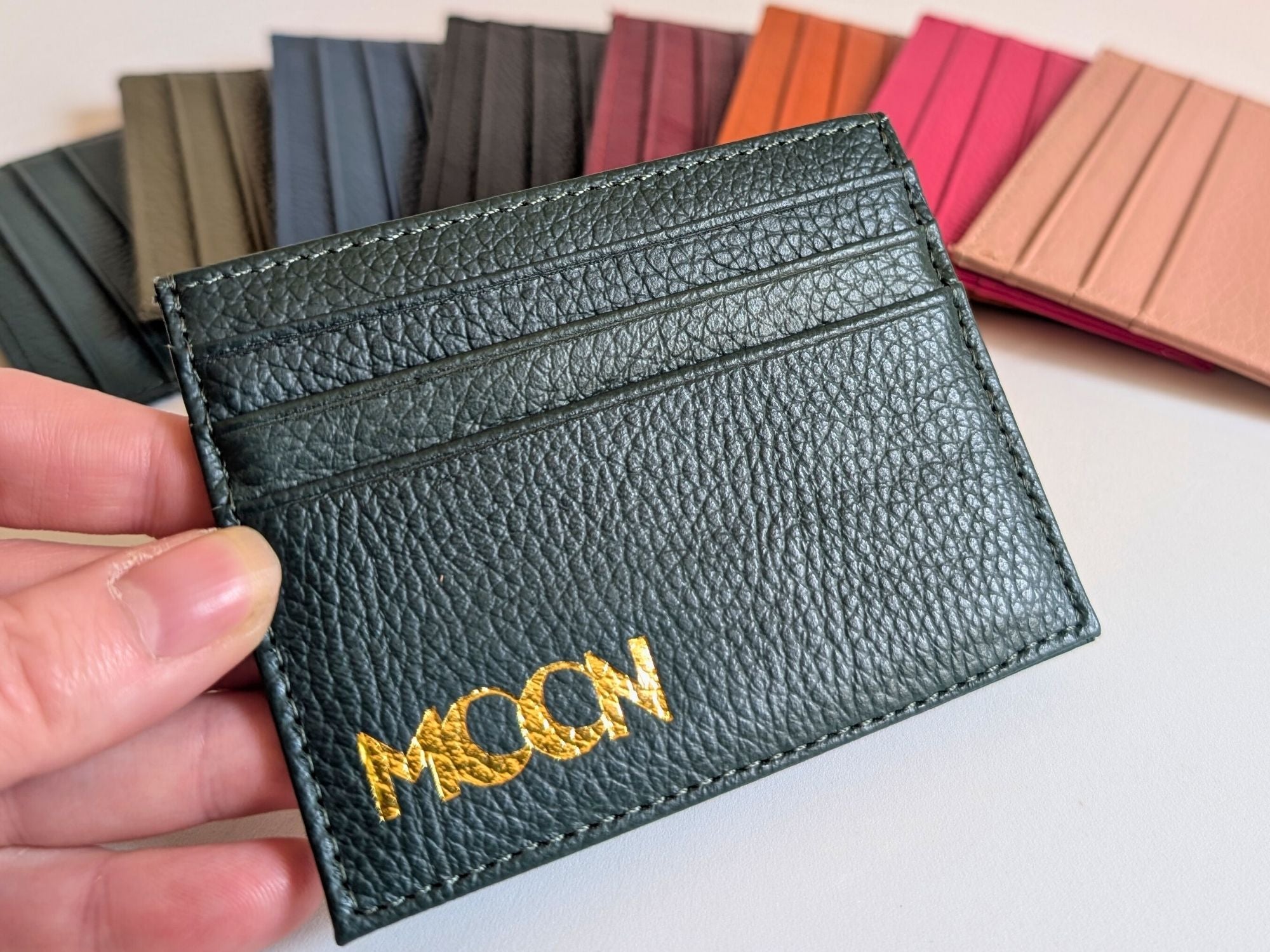 Black leather cardholder with custom emobssed logo held by a hand, with color swatches in the background.