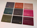 Collection of leather card holders in various colors with initials engraved on a light gray background.