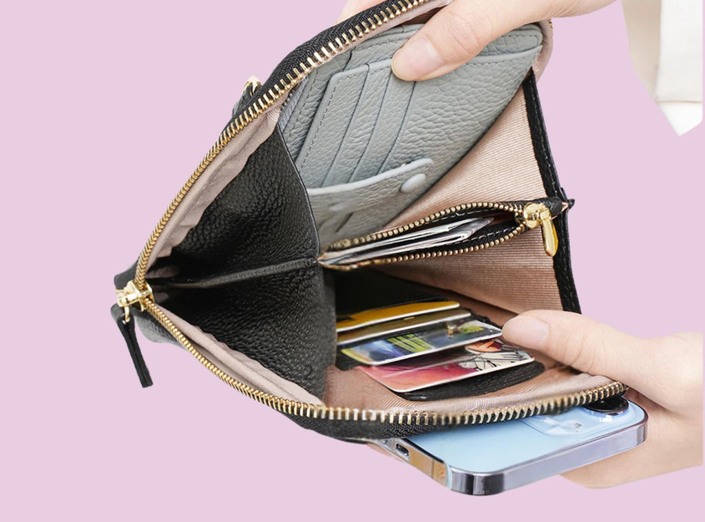 Hand holding a black leather wallet with cards and a phone on a pink background