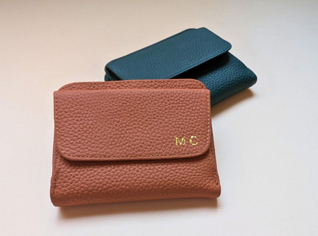 Brown leather wallet with gold initials and teal wallet on a light beige background