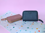 Two wallets, one pink and one black, on a colorful polka dot surface with a pink background.