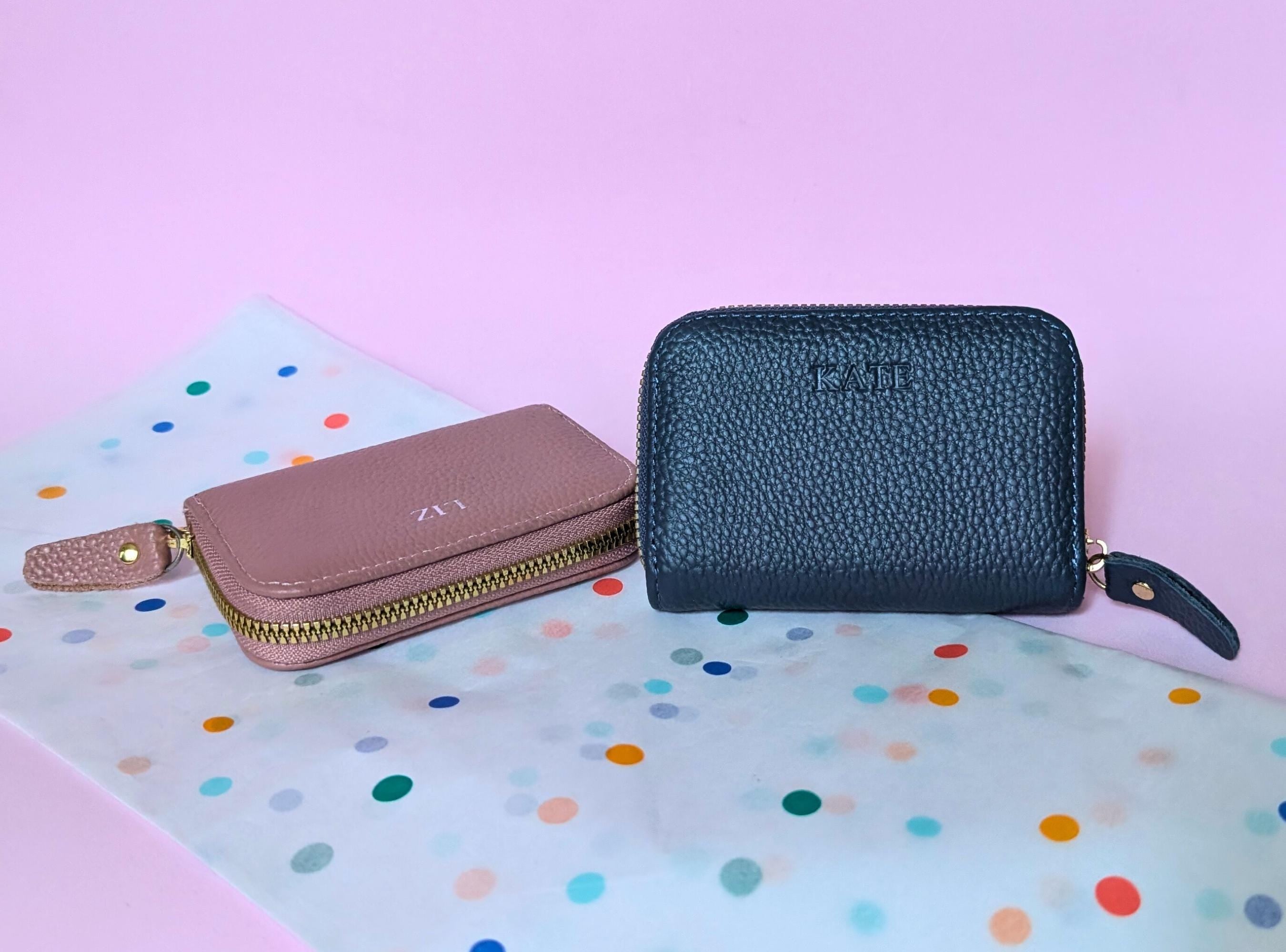 Two wallets, one pink and one black, on a colorful polka dot surface with a pink background.