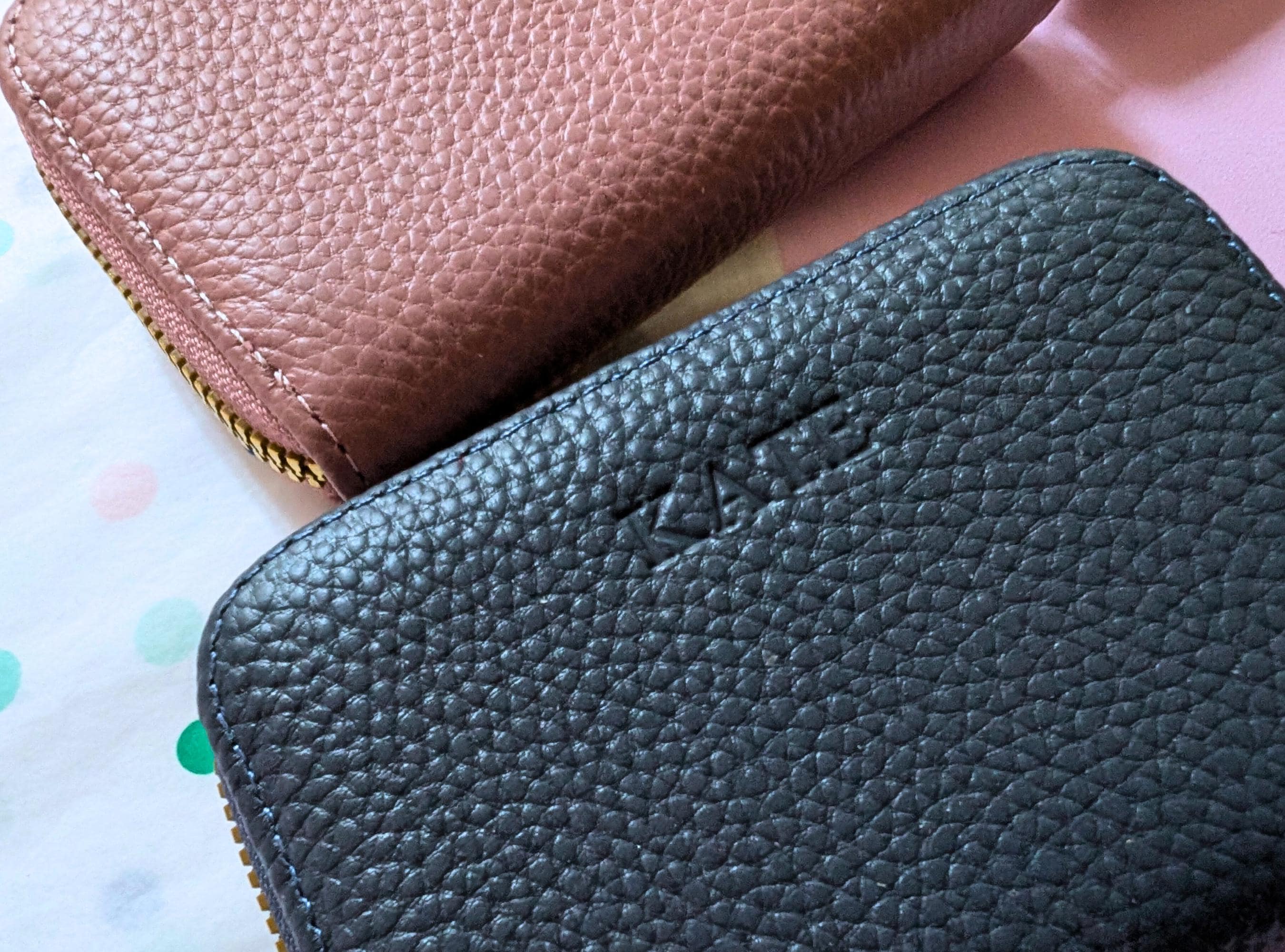 Close-up of a black textured wallet with a brown one partially visible on a polka dot surface.