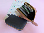 Two zippered wallets, one black and one pink with card slots, on a polka dot background.