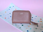Pink textured wallet with custom initials or personalized branding on a polka dot background