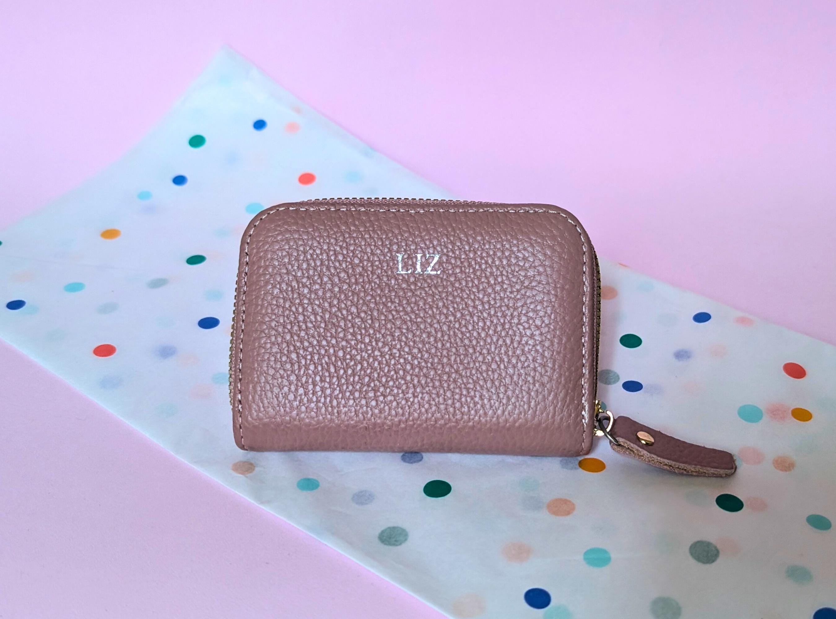 Pink textured wallet with custom initials or personalized branding on a polka dot background