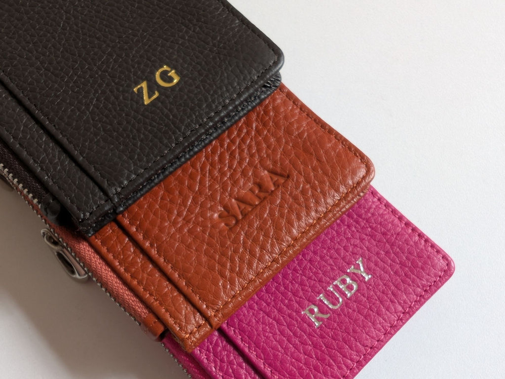 Close up of three leather card holders in black, brown, and pink showing the custom emboss.