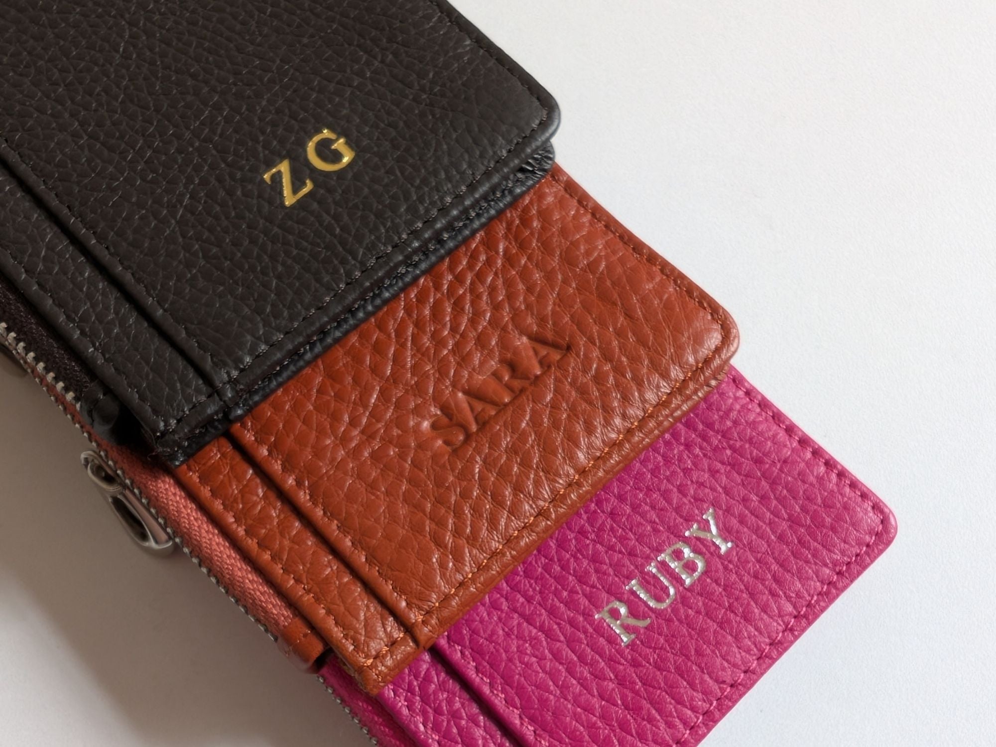 Close up of three leather card holders in black, brown, and pink showing the custom emboss.