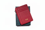 Red leather cardholder with gold initials on a black box against a white background